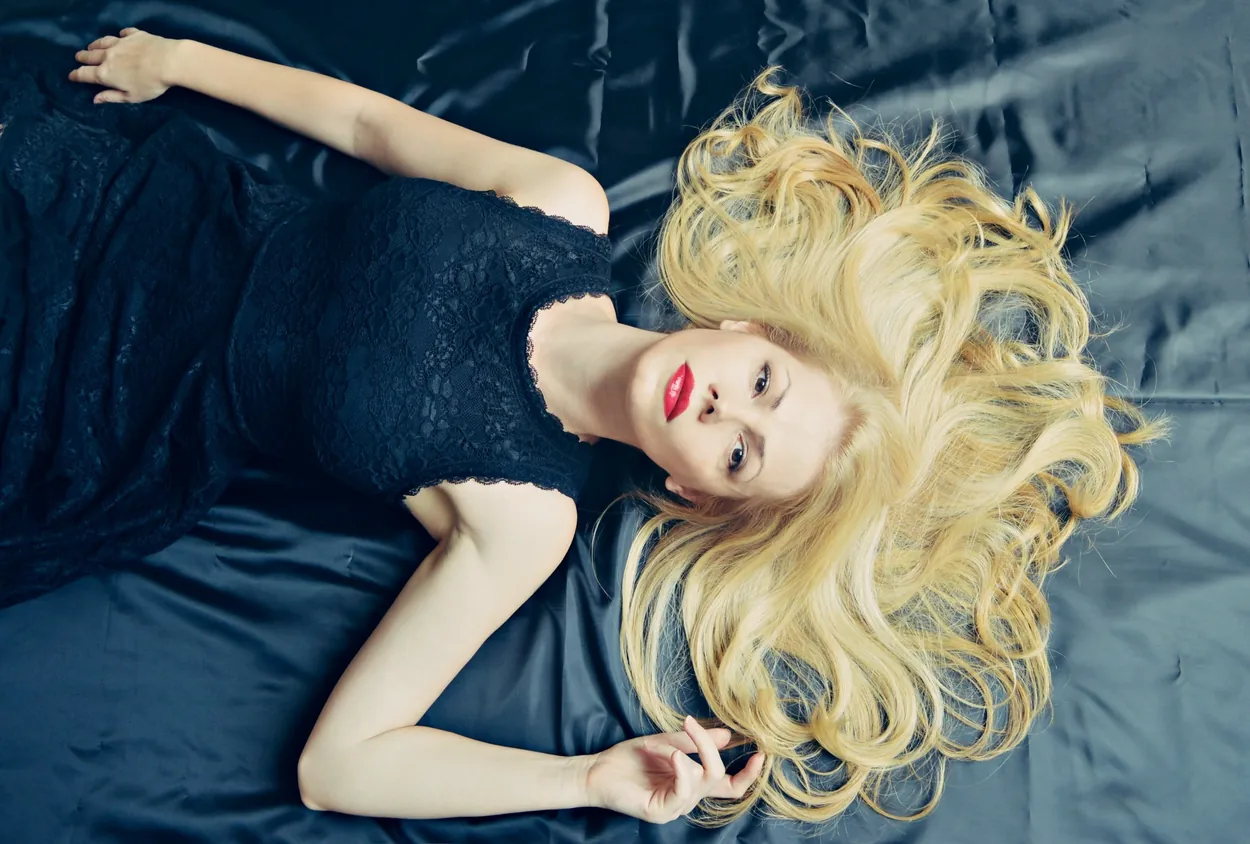 Blonde model reclining on dark satin in a black lace dress