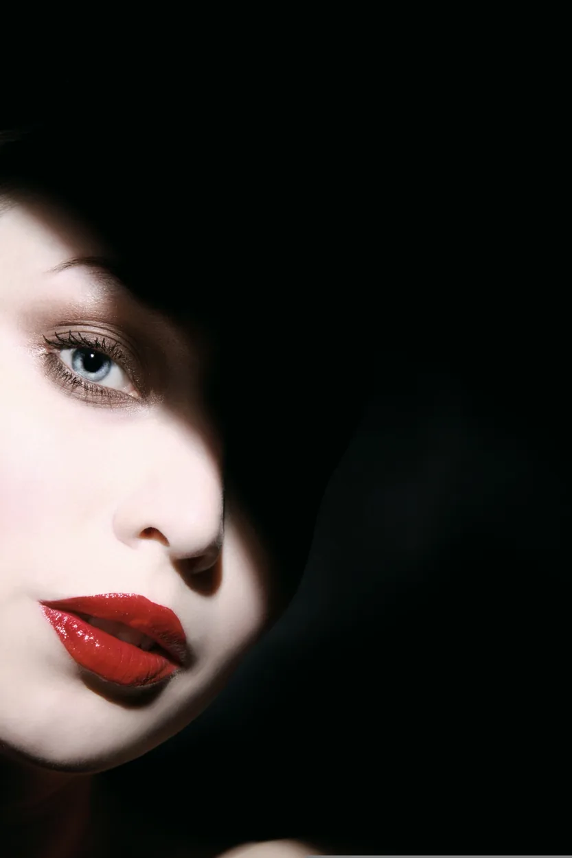 Beauty close-up with red lipstick emerging from dramatic black shadow